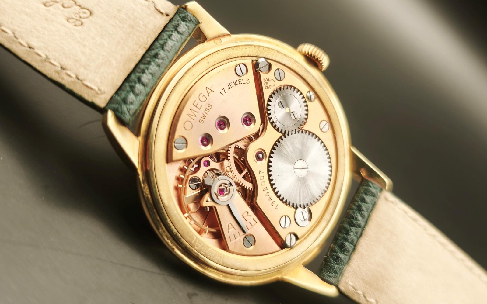 Vintage Omega Caliber 266 mechanical watch movement showing brass mechanism, intricate gears, balance wheel, handcrafted components with 17 jewels, and Incabloc shock protection from 1952