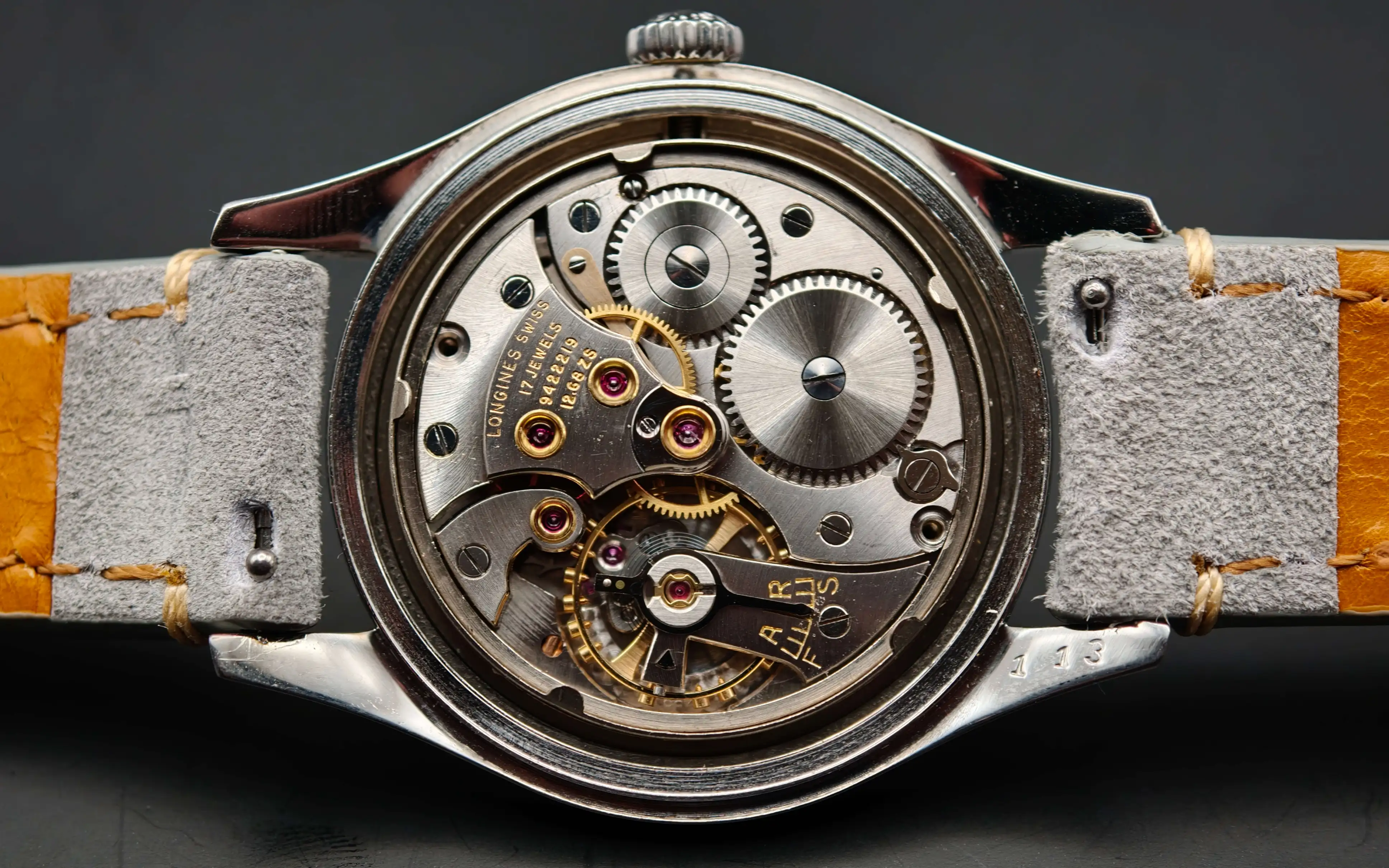 Vintage Longines Caliber 12.68 ZS mechanical watch movement showing nickel-finished mechanism, intricate gears, balance wheel, handcrafted components with 17 jewels, and shock protection from 1954