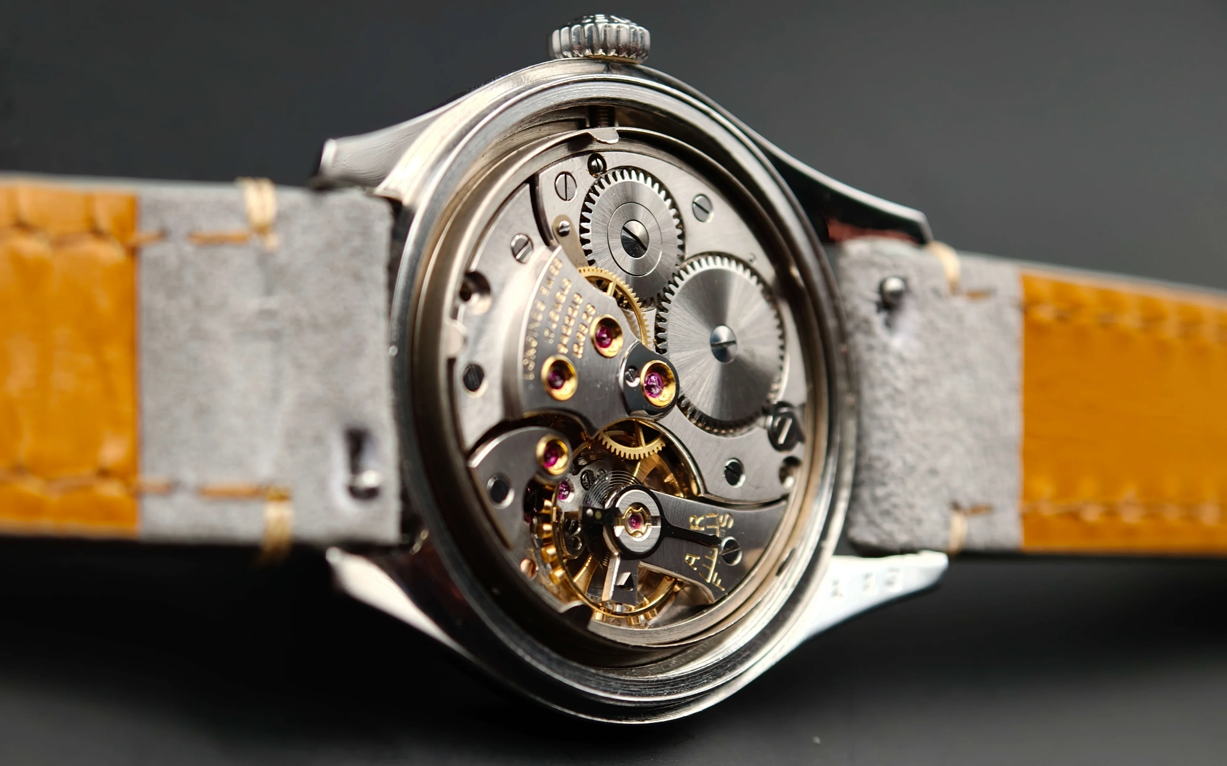 Vintage Longines Caliber 12.68 ZS mechanical watch movement showing nickel-finished mechanism, intricate gears, balance wheel, handcrafted components with 17 jewels, and shock protection from 1954.