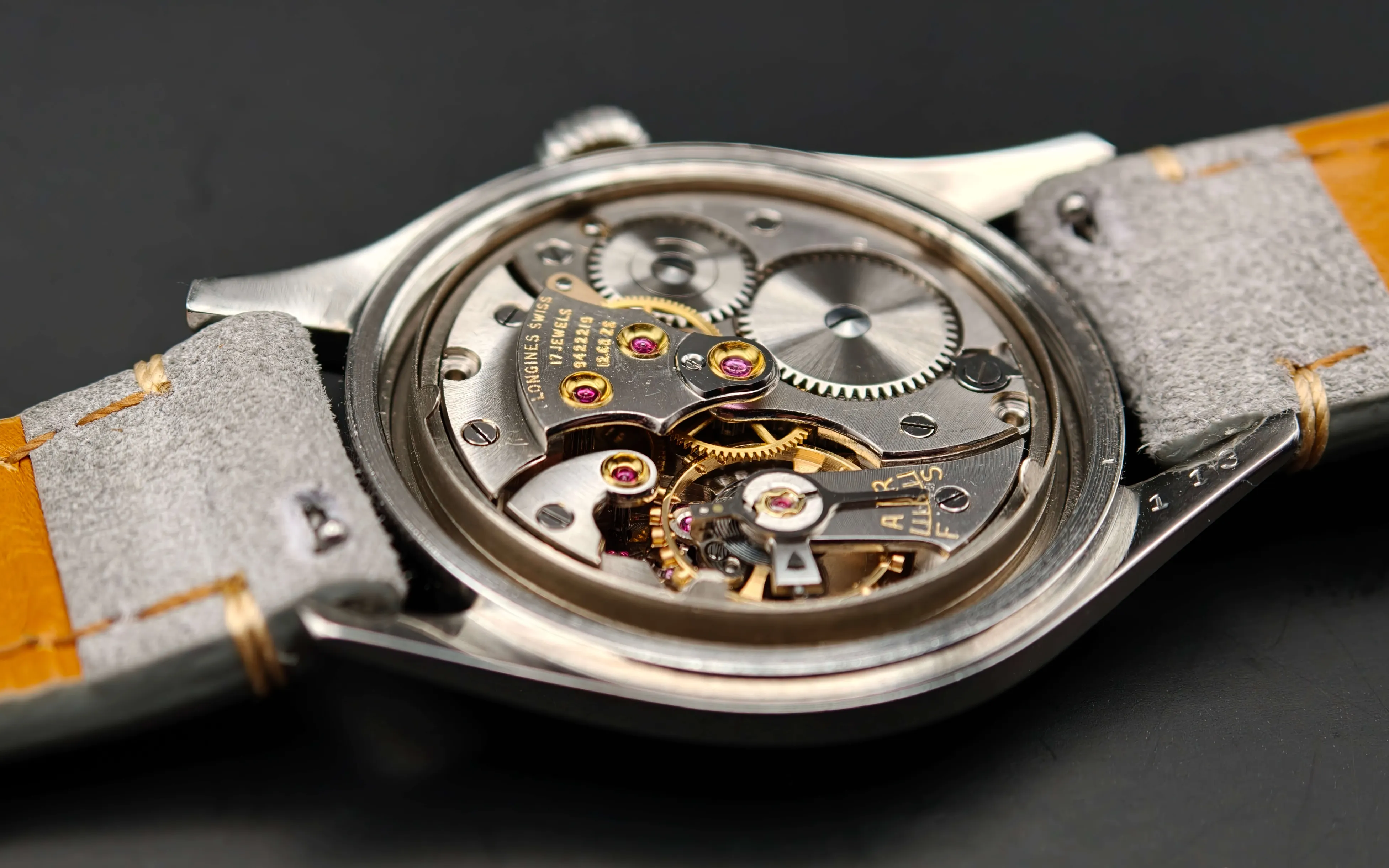 Vintage Longines Caliber 12.68 ZS mechanical watch movement showing nickel-finished mechanism, intricate gears, balance wheel, handcrafted components with 17 jewels, and shock protection from 1954.