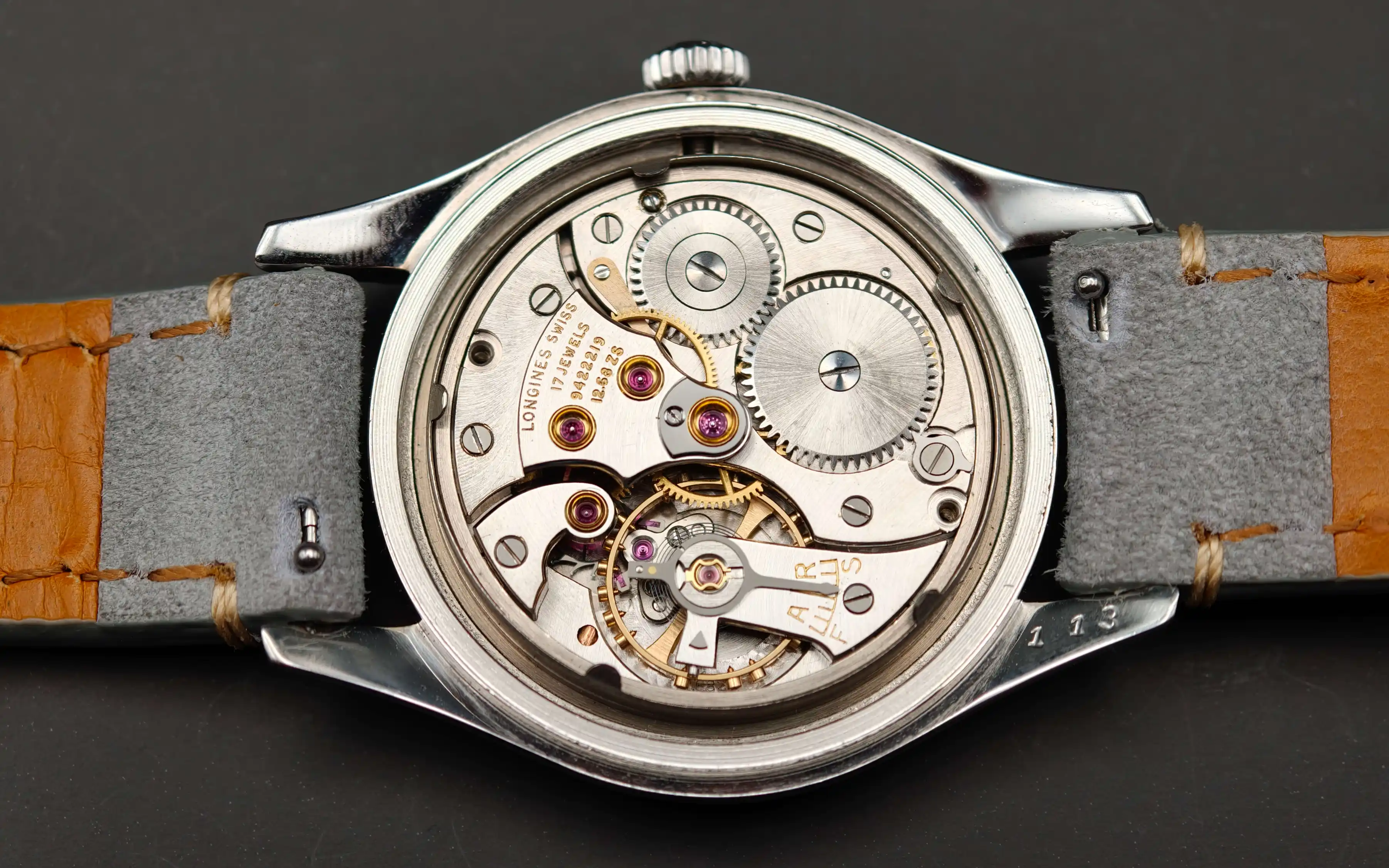 Vintage Longines Caliber 12.68 ZS mechanical watch movement showing nickel-finished mechanism, intricate gears, balance wheel, handcrafted components with 17 jewels, and shock protection from 1954.
