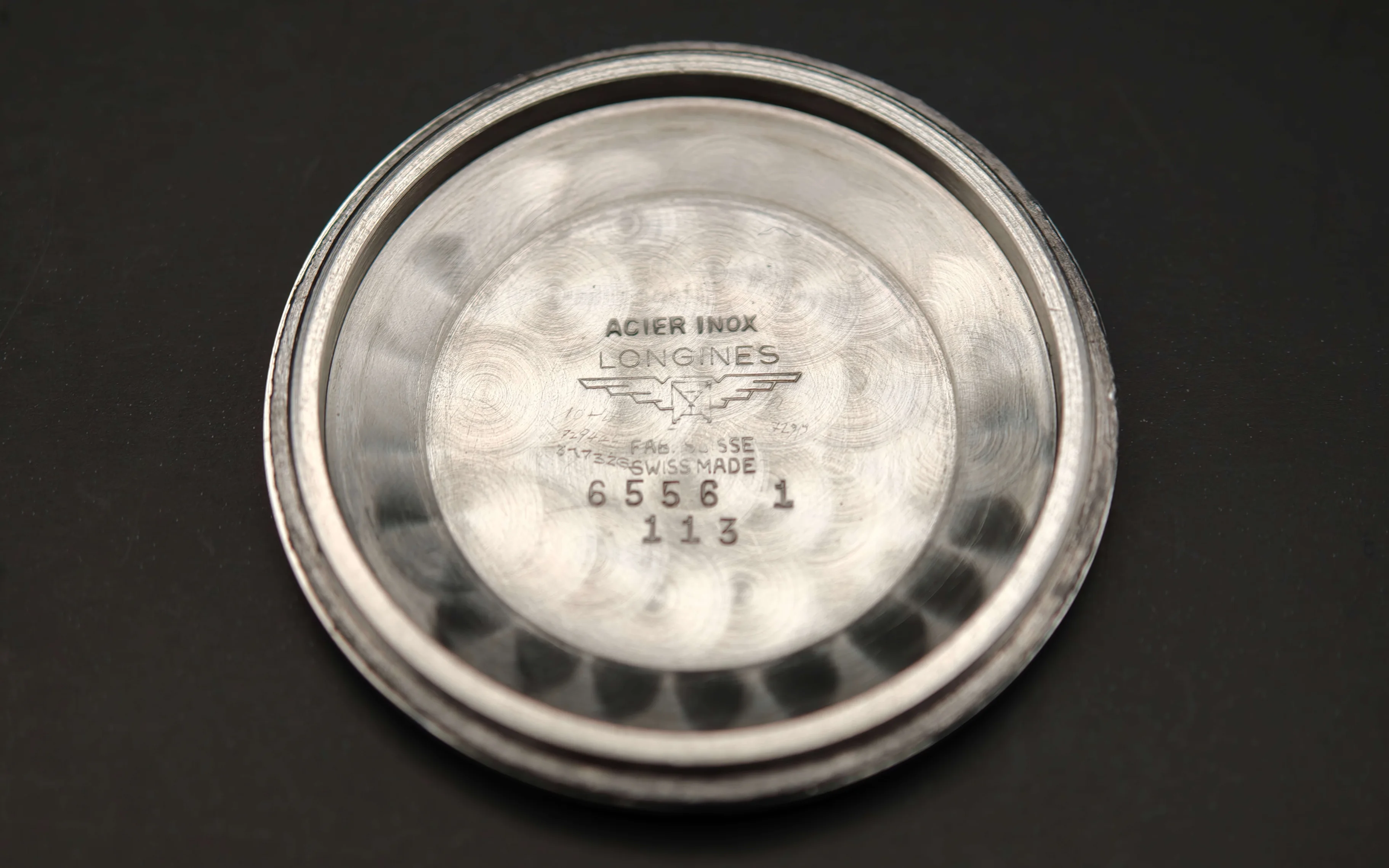 Vintage Longines stainless steel watch case back from 1954 showing hallmarks, reference number 6556, engraved details, steel patina, and vintage watch authentication marks from private watch collection.